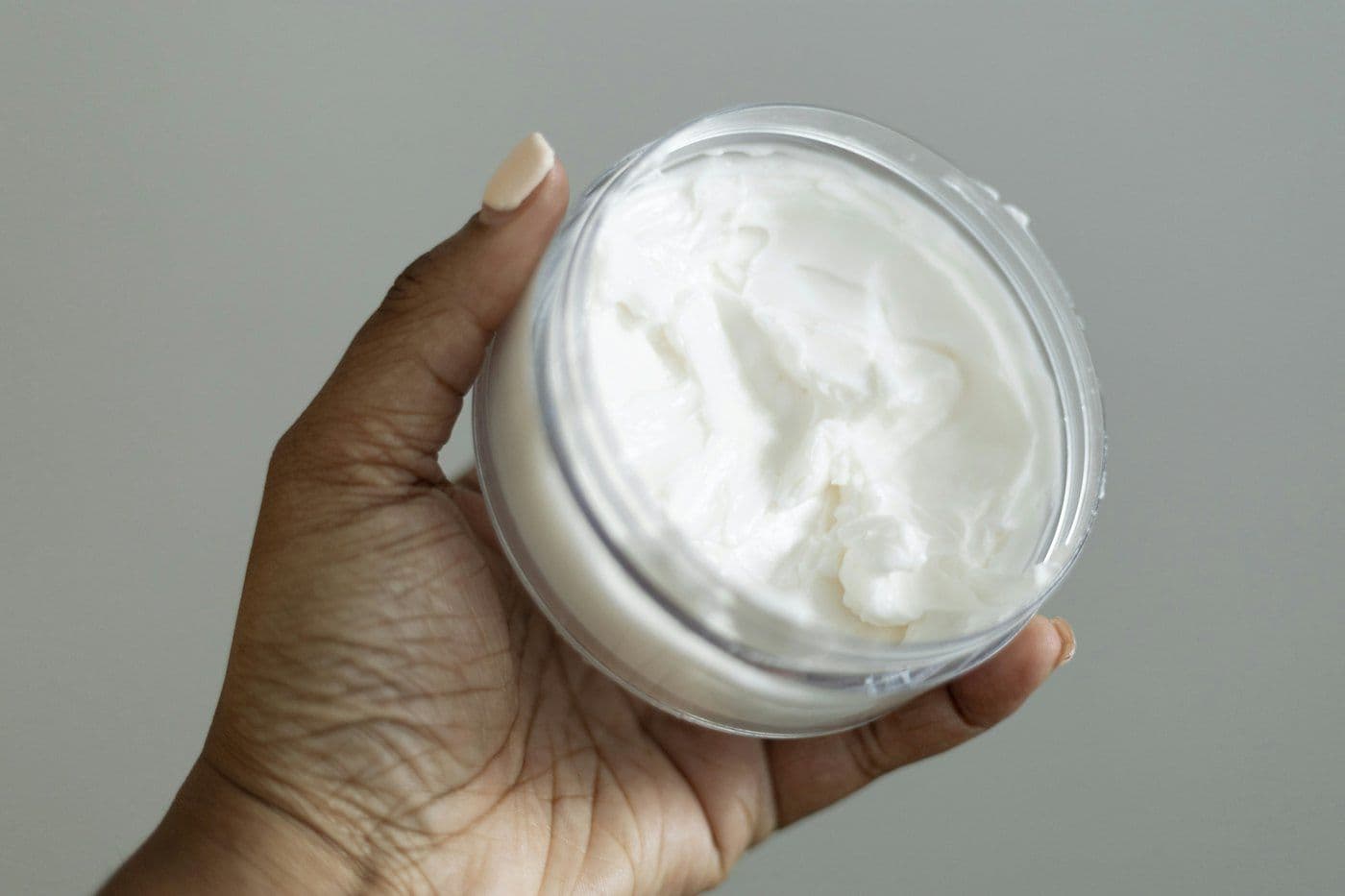 A hand holding an open jar of face cream